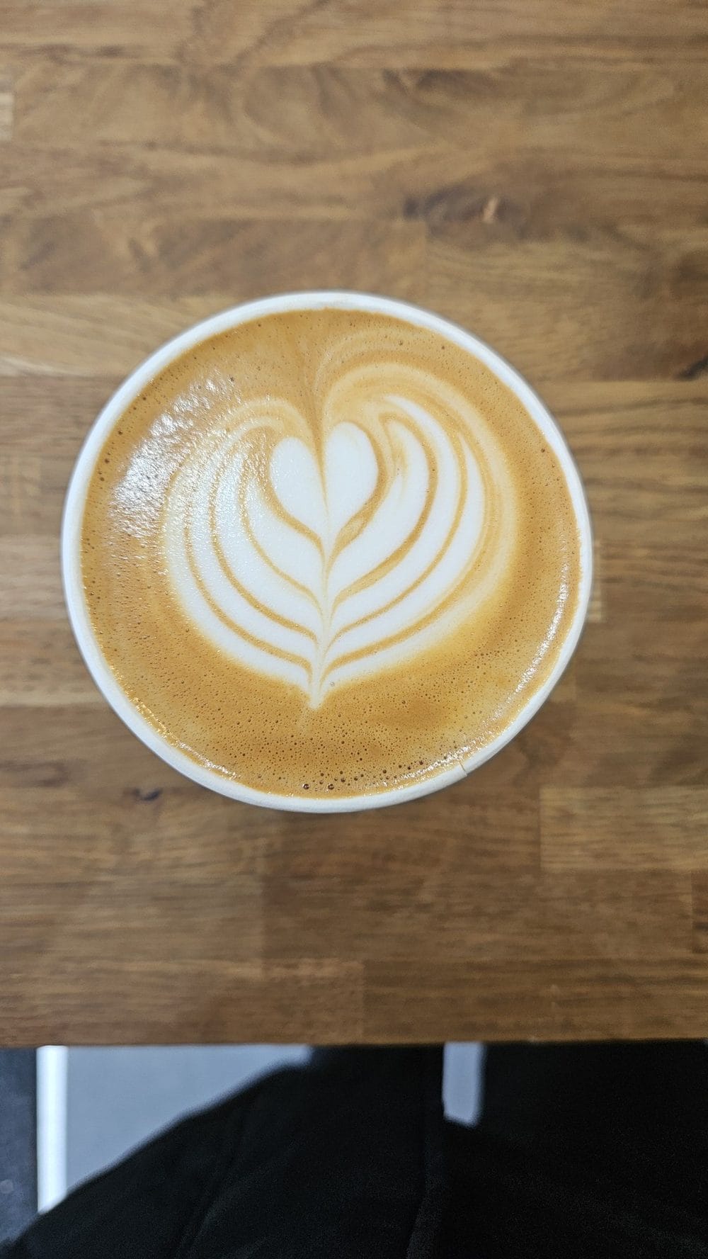 A flat white with latte art on a warm wooden counter at Lytte Coffee